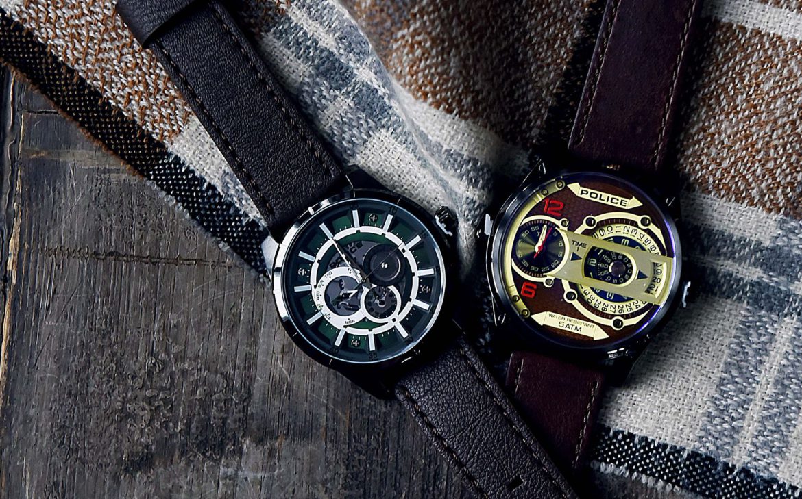 Na odzieży w kratkę leżą dwa eleganckie zegarki męskie.