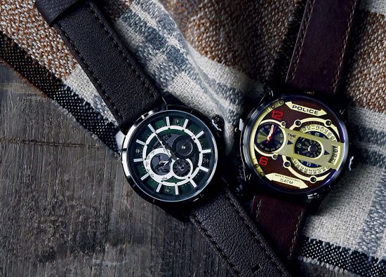 Na odzieży w kratkę leżą dwa eleganckie zegarki męskie.