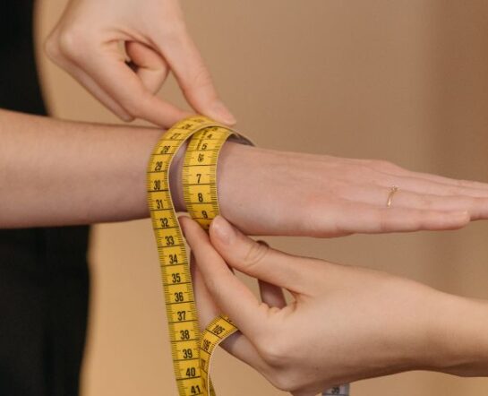 Jak zmierzyć nadgarstek do zegarka? Na zdjęciu jedna koboeta owija miarkę wokół nadgarstka drugiej kobiety.