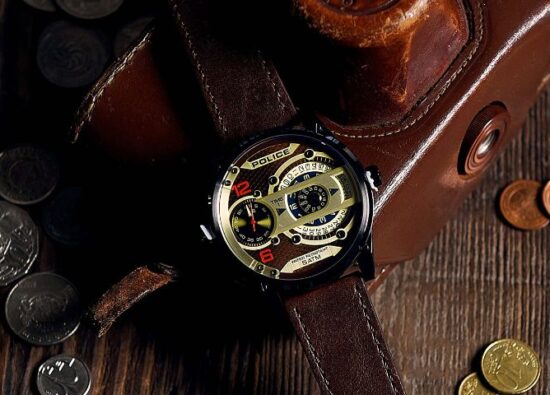 Luksusowy zegarek męski na pasku w otoczeniu monet na drewnianym blacie.