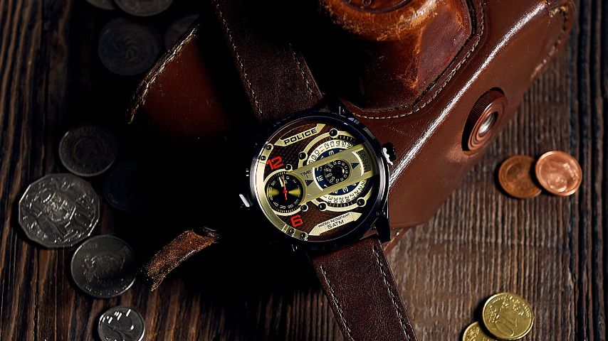 Luksusowy zegarek męski na pasku w otoczeniu monet na drewnianym blacie.