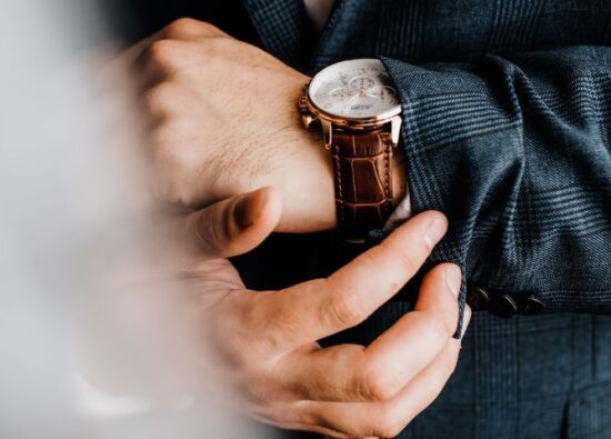 Mężczyzna w garniturze ma na nadgarstku zegarek na ślub. Na pierwszym planie fragment sukni panny młodej.