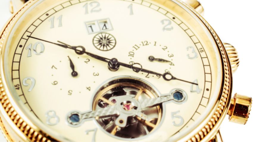 Złoty zegarek z widocznym mechanizmem w dolnej części tarczy.