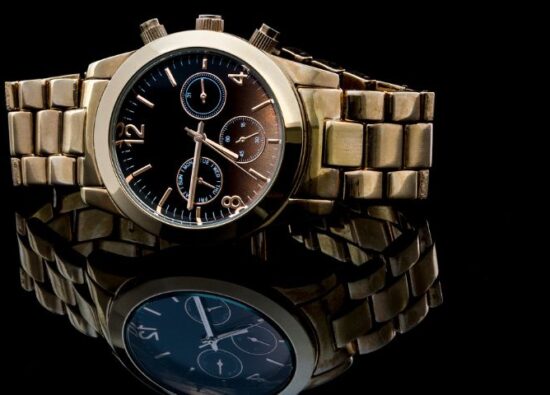 Elegancki, złoty zegarek męski na bransolecie na czarnym tle z odbiciem w szklanym blacie.