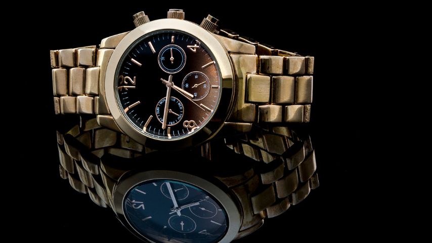 Elegancki, złoty zegarek męski na bransolecie na czarnym tle z odbiciem w szklanym blacie.