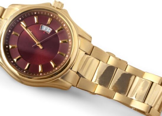Złoty zegarek damski z czerwoną tarczą na białym tle.